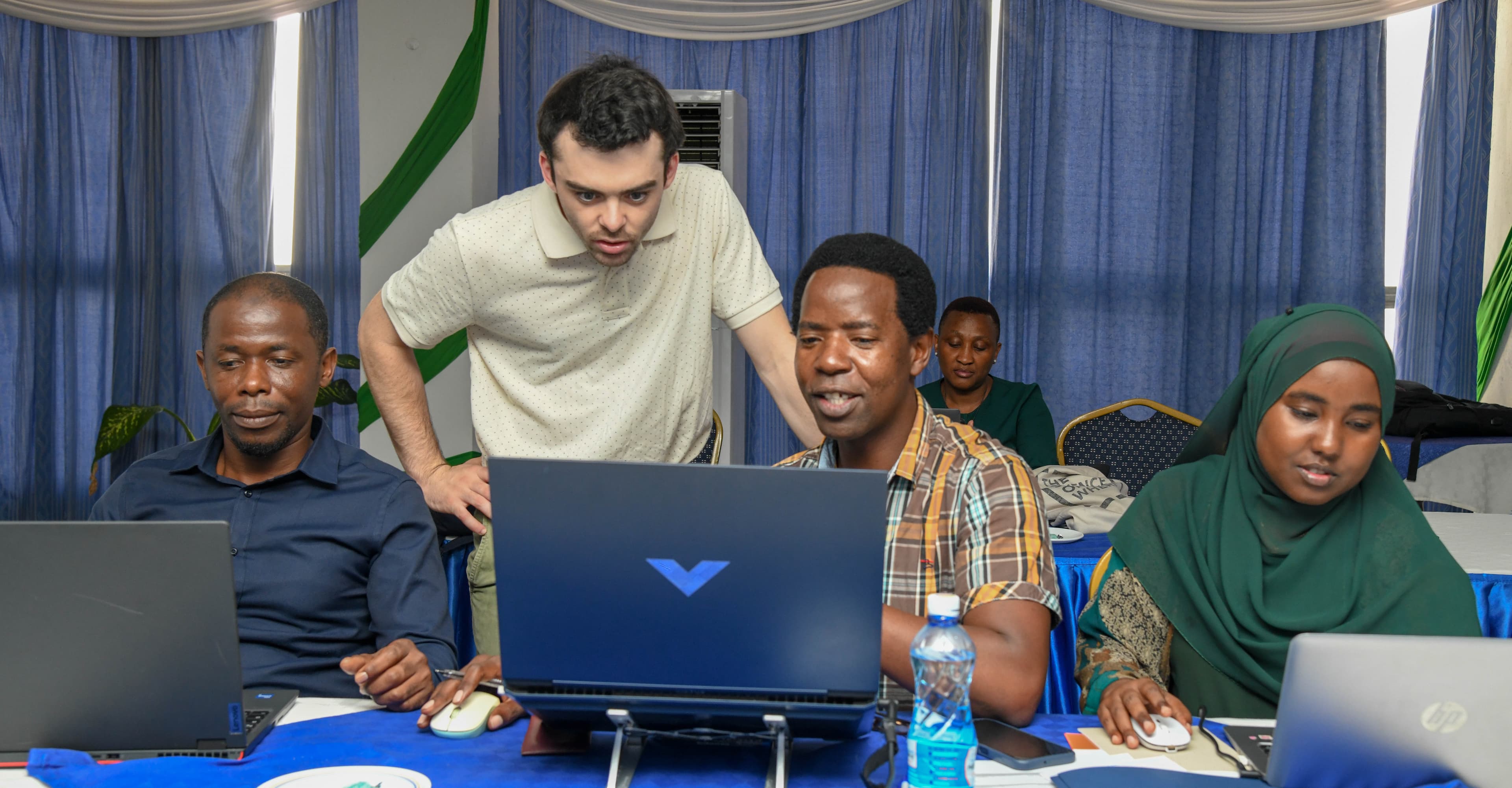 Trident Tools instructor leaning over to assist a workshop participant at a laptop during a hands-on satellite-derived bathymetry software training session