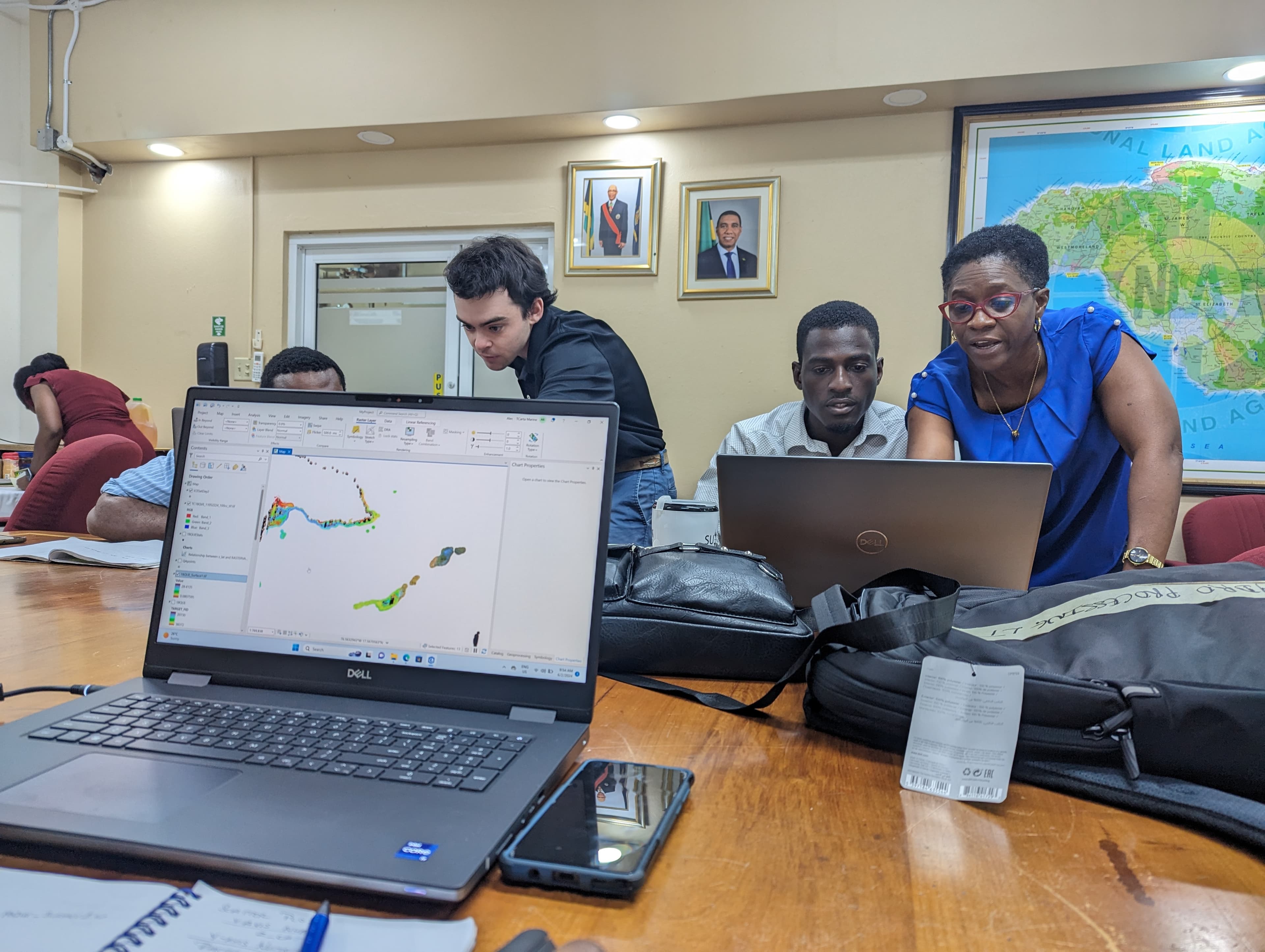 TCarta instructor and Jamaican participants working collaboratively around laptops displaying satellite-derived bathymetry data in ArcGIS during an SDB integration training session
