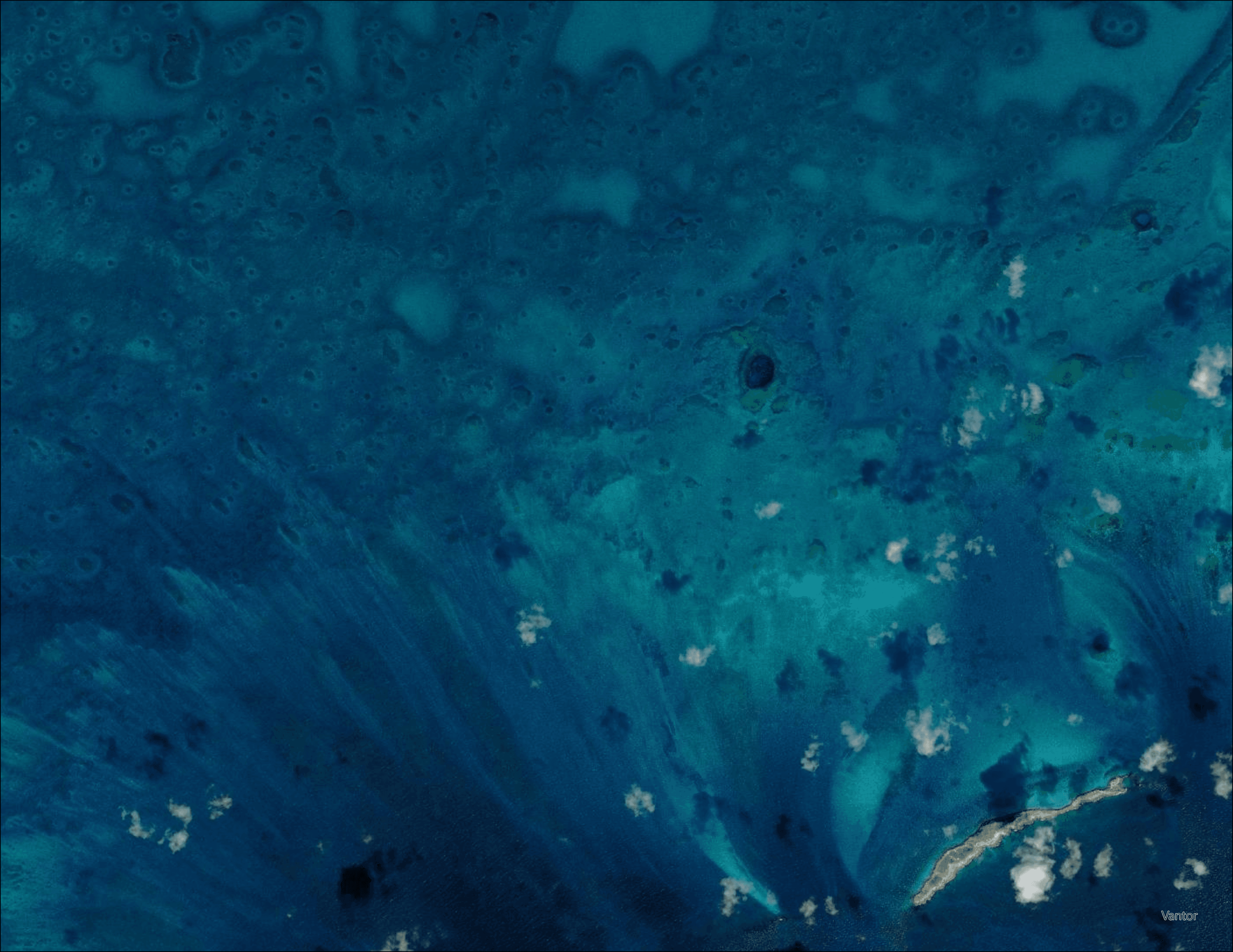 True-color satellite imagery of South Exuma shallow bank showing seagrass and reef features visible through deep blue water with scattered cloud shadows, used as input for seagrass mapping